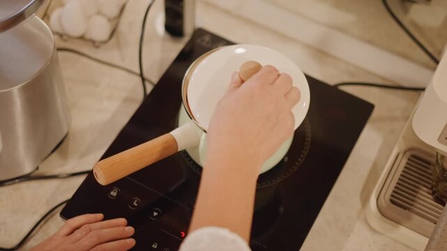 Baker seals lid while pumpkin simmers, induction cooktop display showing controls, neat countertop, enamel pot of orange pumpkin chunks simmering to soften before mashing, minimalist modern kitchen