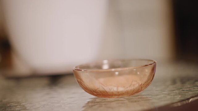 Closeup glass bowl on counter with pumpkin pie crumbs, soft warm light, blurred ceramic mug in background, rustic tabletop texture, quiet home baking atmosphere, gentle bokeh and amber tones