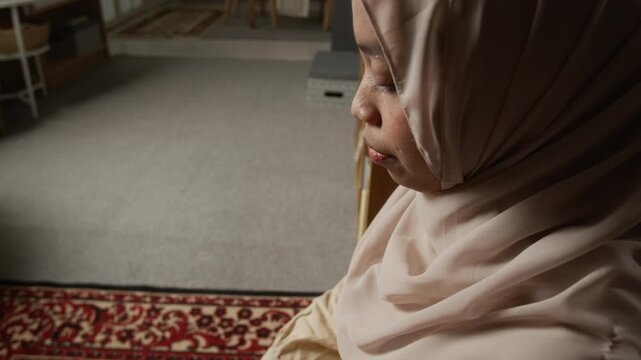 Cinematic detail shot of Muslim young woman wearing modest clothing and performing salah finishing daily praying ritual in serene home setting, copy space