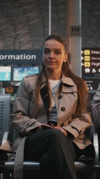 Young Stylish Woman Sits in Busy Airport Lounge, Visibly Uncomfortable Among Noisy Strangers. Social Anxiety, Struggle of Introvert in Public Spaces, and Need For Solitude in Crowd. Vertical Shot.