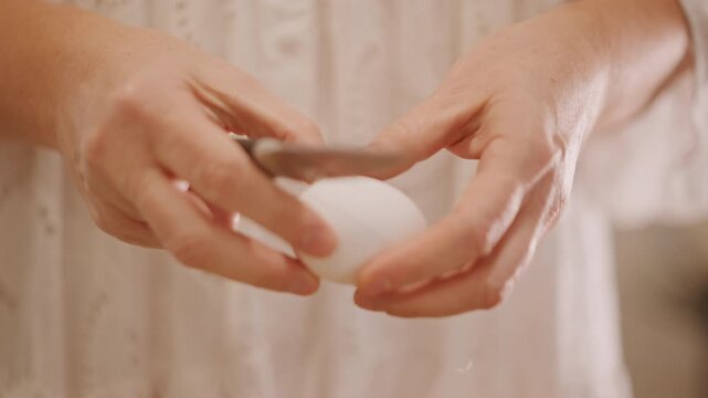 Soft lit hands holding egg, gentle knife scoring shell, warm kitchen backdrop, preparing eggs for pumpkin pie filling, cozy autumn mood, closeup texture and steady motion for recipe footage.