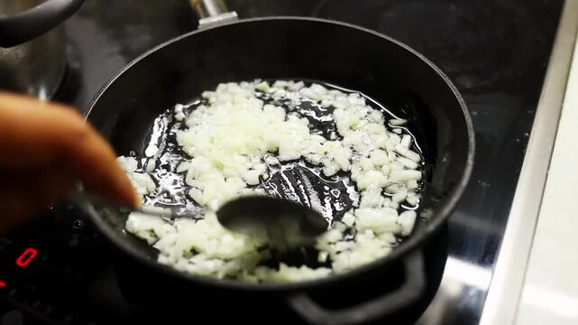 Man's hand stirring blanching onions in frying pan on stove at home