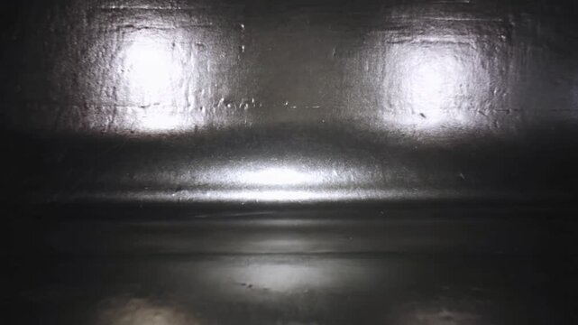Shifting reflections on glossy metal panel after camera tilt in box, showing seam and highlights
