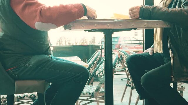 Two unrecognizable senior men talking while seated at a cafe table near a window