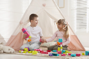 Little kids playing with building blocks near toy wigwam at home © New Africa