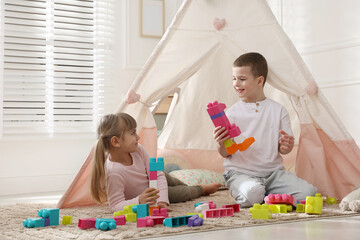 Little kids playing with building blocks near toy wigwam at home © New Africa