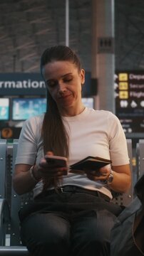Stylish Female Traveler Sits In Departure Lounge, Holding Boarding Pass And Red Apple. Woman Enjoys Healthy Snack While Scrolling Through Smartphone. Balanced Lifestyle, Travel Habits. Vertical Shot.