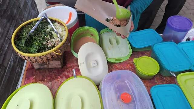 PAMEKASAN, INDONESIA - DECEMBER 15, 2025: Handheld footage of a street food vendor preparing nasi pecel orders, traditional Indonesian cuisine with vegetables and peanut sauce, capturing authentic loc