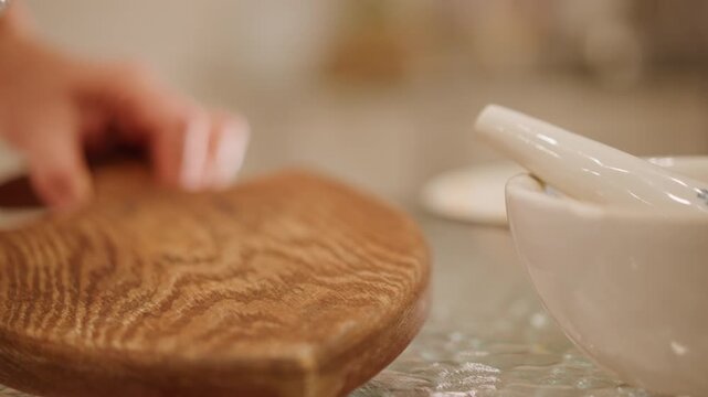 Closeup mortar and pestle on table hand placing glass bowl of chopped pecans onto wooden board beside ceramic mortar, soft shallow depth, warm kitchen lighting, finishing touch for pie topping