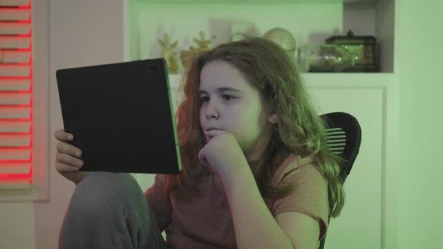 Gamer child watches tablet closely. Gamer kid plays casual gameplay. Gamer child enjoys digital leisure. Gamer kid relaxes with gaming.