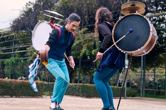 Adult couple of urban dancers, happily playing and dancing the cueca with a bass drum on their backs outdoors, Chilean chinchineros, street musicians who play the bass drum and dance in the streets.