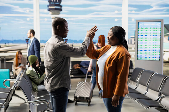 Relieved comic parents waving goodbye to daughter and sharing high-five, celebrating empty nest milestone with upbeat lighthearted expressions. Job done concept and freedom in airport.