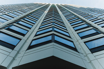 Obraz premium View of a tall building from the ground looking up at the windows and sky showing the angle of the architecture against the blue background
