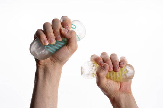 Two hands squeezing transparent textured masturbator sleeves with colored inner ribs, isolated on white background.