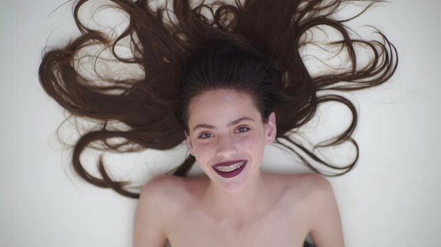 Girl laughing funny face with braces and teeth. Teen girl portrait closeup smiling with dental braces. Young woman laughing lying down top view. Cute teen girl smiling cheerful with natural beauty.