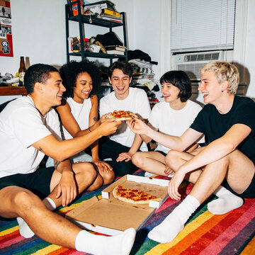 Authentic candid shot of diverse Gen Z friends laughing and sharing pizza in a cozy messy apartment, Y2K aesthetic direct flash photography