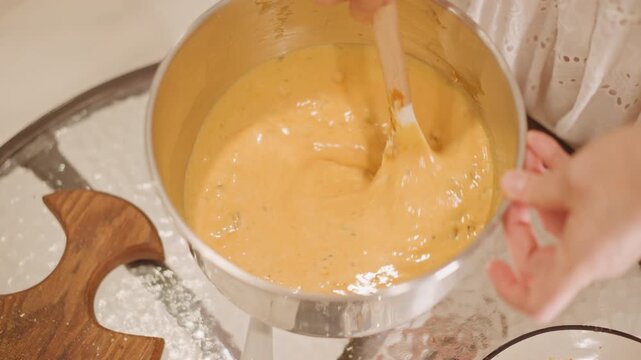 Silky pumpkin custard being gently stirred, stainless bowl on flour dusted table, spatula folds glossy batter, speckled spices visible, precise circular motion, calm domestic pastry scene showcasing