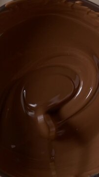 Slow motion macro shot of melted chocolate being stirred with a spoon in a bowl. Liquid smooth chocolate texture, food background, dessert preparation, bakery concept. Rich and indulgent mood. Close-u