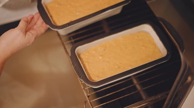 Two pumpkin loaves arranged in oven, rectangular pans on rack, careful baker sliding tray, warm spice aroma suggested, dual loaf batch for holiday treats, efficient kitchen routine