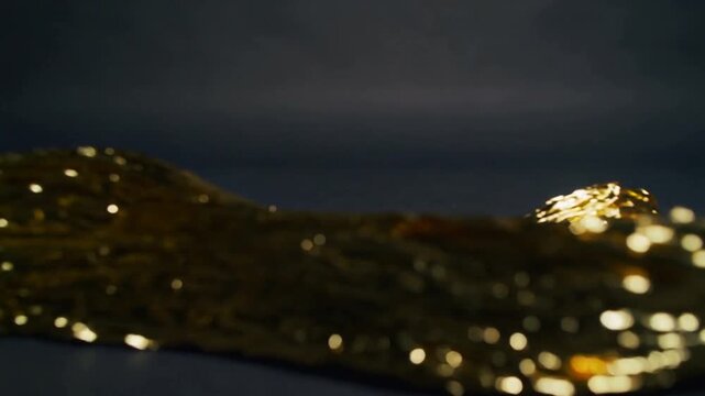 Rippling metallic gold ribbon creasing and scattering flecks on dark tabletop under studio lights