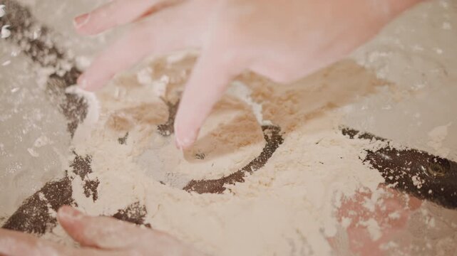 Closeup of baker molding pumpkin crust. Focused image of hands forming pie dough with flour clouds. Intimate view of baker pressing cutter into dough with precise motion and flour accents