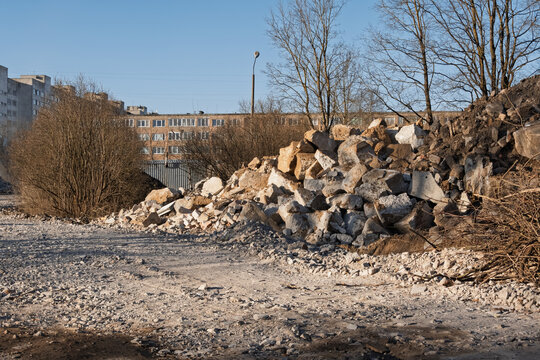 Large piles of concrete debris and foundations at a building demolition site in Narva, Estonia. Urban landscape with residential buildings in the late afternoon spring sun.