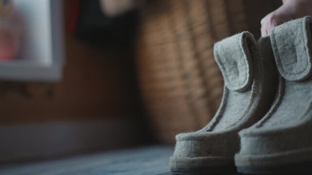 Cozy home morning by window slippers sit on wooden floor, person slips into wool boots next to woven basket, soft natural light, quiet domestic ritual, rustic textures and subtle motion