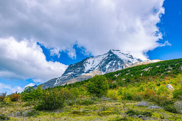 Snow-covered mountain beneath dramatic clouds with green hills and vegetation in Torres del Paine National Park, Patagonia, Chile. © ZL Visuals