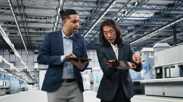Multiethnic management executives use device to examine semiconductor substrate in cleanroom. Teamworking colleagues verify optical photolithography patterns on silicon wafers with tablet, camera A