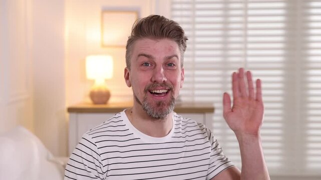 Smiling man in striped t-shirt waving hello at home