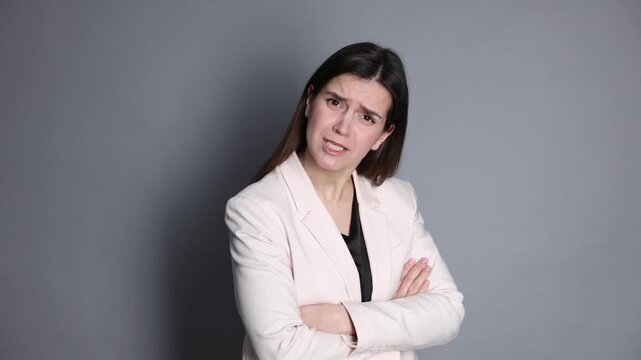 Resentful businesswoman in suit crying on grey background