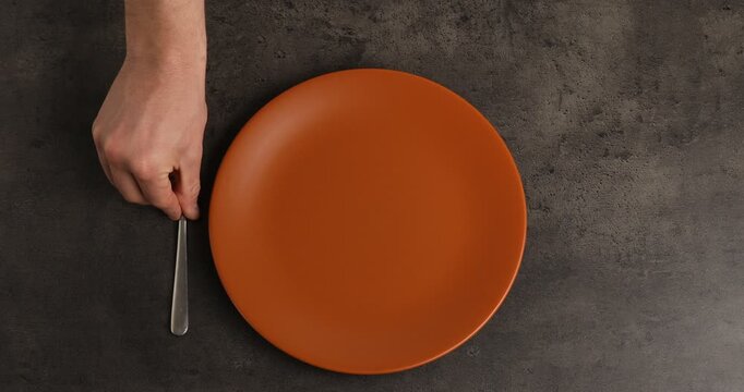 Man putting plate and cutlery onto grey table, top view