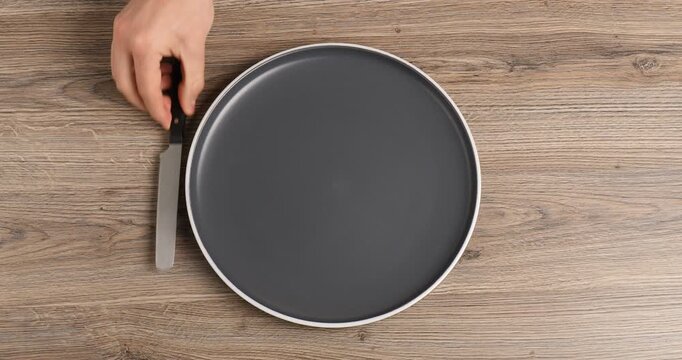 Man putting plate and cutlery onto wooden table, top view