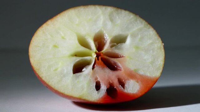 Dropping red stream, liquid filling star core in halved red apple on white surface, studio lighting