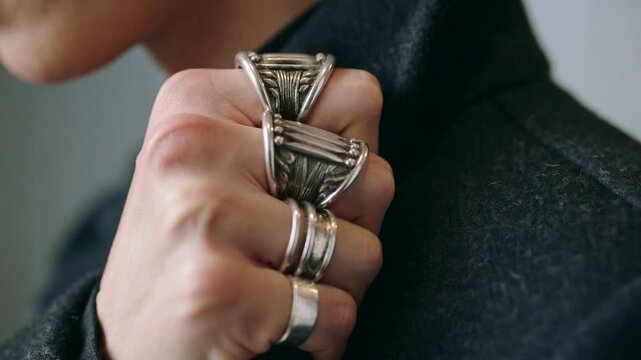 Man placing fist on coat lapel and rotating hand, highlighting silver rings for fashion showcase