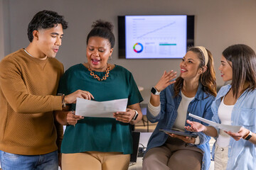 Diverse coworkers reviewing papers and tablet in office with wall display, in casual attire © wavebreak3