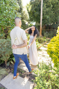 Couple holding hands walking on stepping-stone path in residential garden, man hiding pale flower