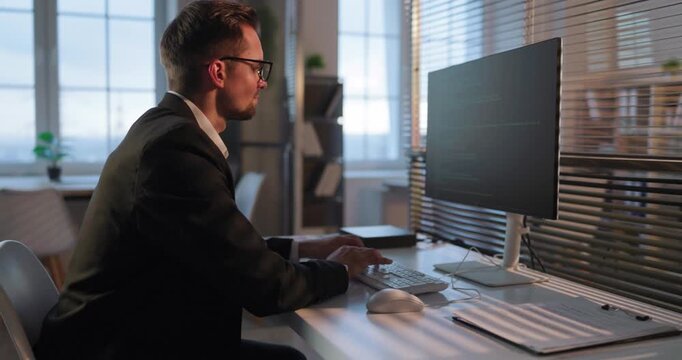 Programmer developer man coding at office computer monitor. Business coder works at keyboard, debugging and reviewing code. Modern workplace concept of technology productivity and focus.