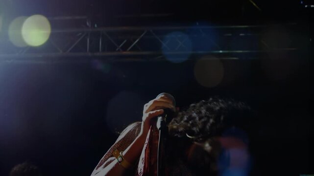 Singer starting singing into mic under lights, whipping hair, lens flares, energizing concert fans