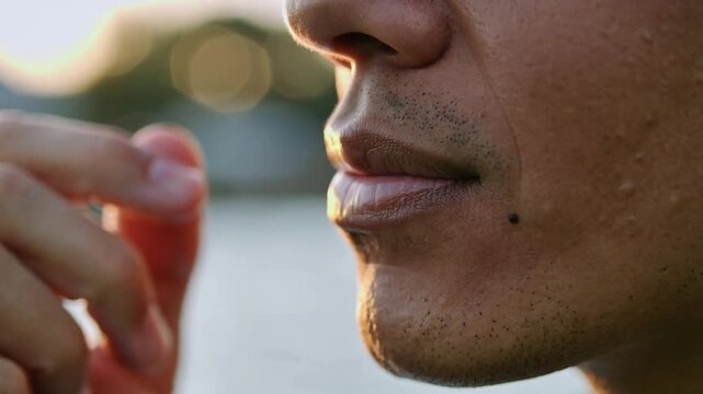 Pressing stubbled man's right fingertip against lower lip, checking chapped lip under late sunlight