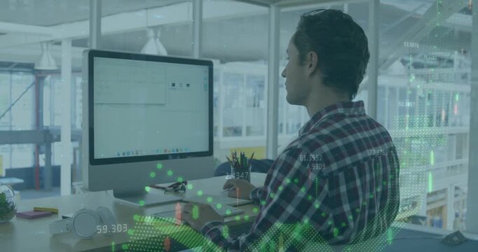 Man sitting desk reviewing business data, causing green graphs overlaying monitor and man