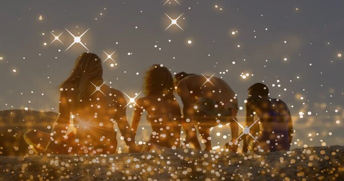 Sparkles appearing at sunset, four figures sitting on sand, third leaning, helping right companion