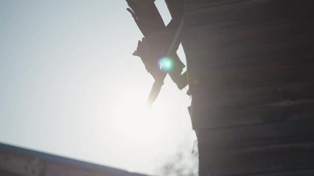 Sunlit home eaves with bright sun, silhouette of broken wooden roof edge, warm backlight and soft flare, rustic texture and dust motes, slow handheld pan suggesting repair and inspection of aged
