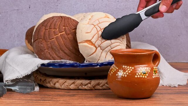 A hand picks up a vanilla concha bread with silicone tongs