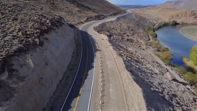 Aerial image of a car driving along Route 40 over the Collon Cura River in Patagonia Neuquen. An action shot with arid landscapes and the transparent river at the edge of the road.
