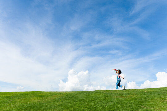 A little girl playing with a toy airplane under a blue sky with white clouds