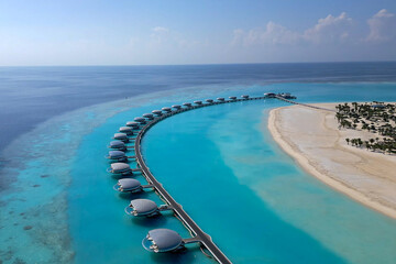 Fototapeta premium Aerial view of futuristic pod-shaped villas connected by a long pier in a turquoise lagoon
