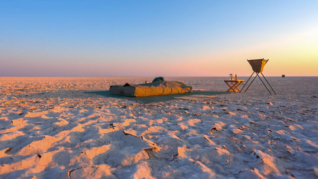 A simple camping setup with a bedroll on a cracked dry desert landscape at golden hour