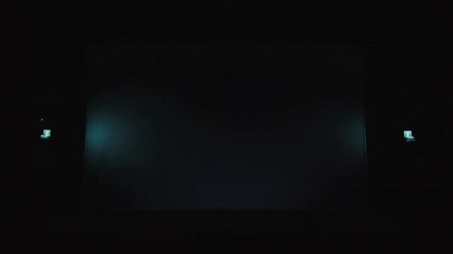 Dimming projector lamp causing projection screen fading at theater, marking show end, with rows