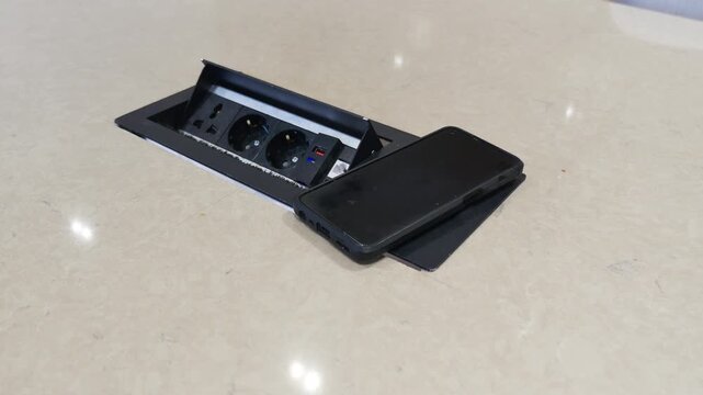 A person places smartphone on black wireless charger next to multi-socket power strip.